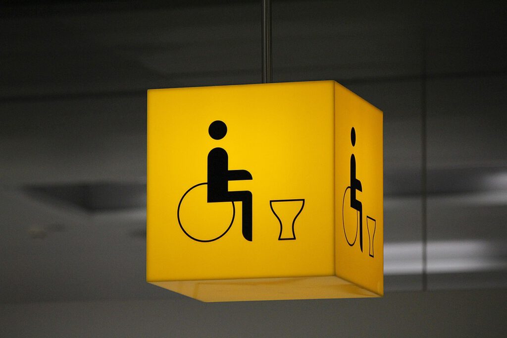 Gelber Neonwürfel mit einem Rollstuhlfahrersymbol samt Toilette drauf.