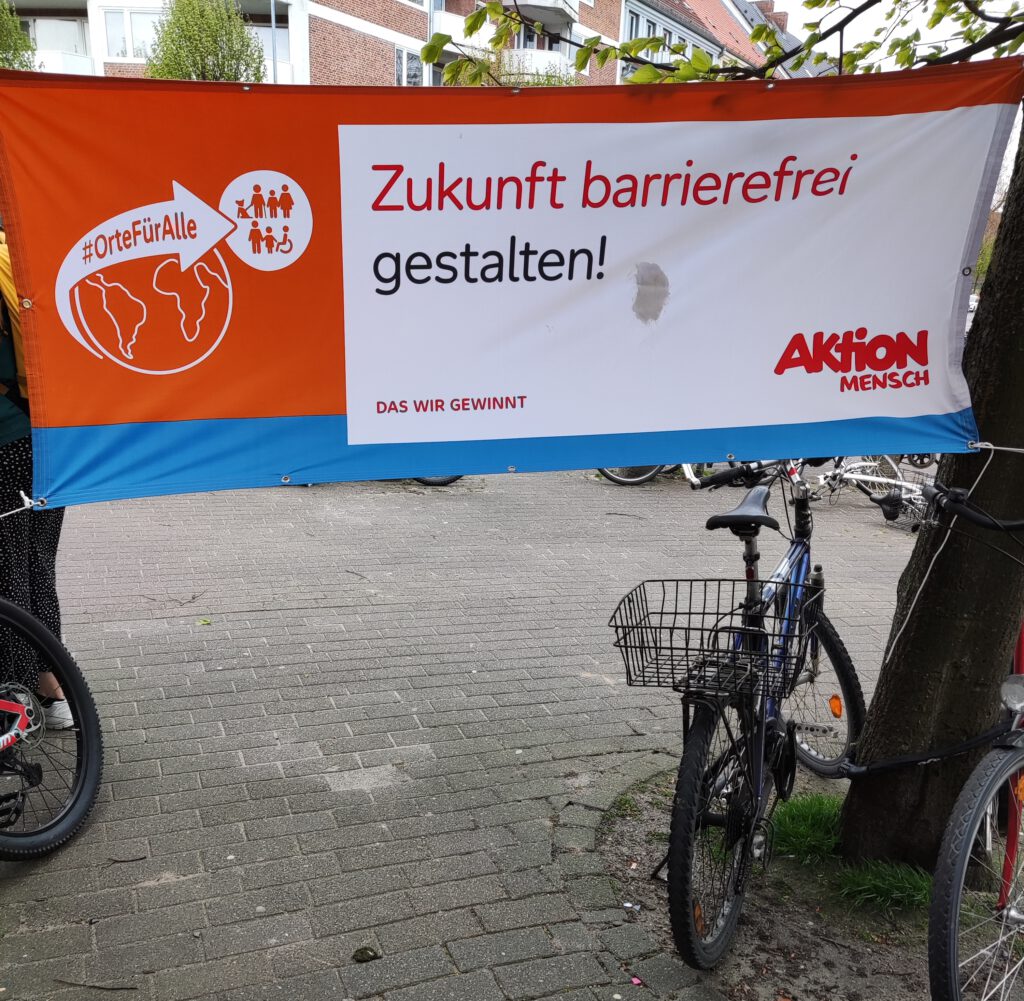 Ein Banner der Aktion Mensch, der an einem Baum befestigt ist. Darauf steht: "Zukunft barrierefrei gestalten".