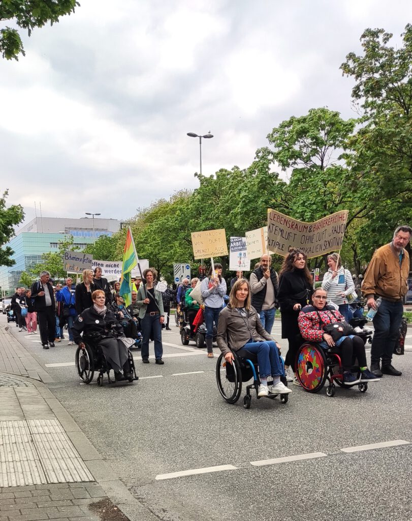 Eine Gruppe von Protestierenden, die durch die Straße ziehen. Im Vordergrund Rollstuhlfahrende.