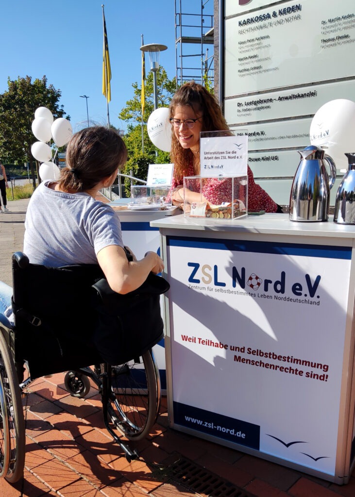 Mitarbeiterin des ZSL Nord e.V. hinter einem Tresen im Gespräch mit einer Besucherin.